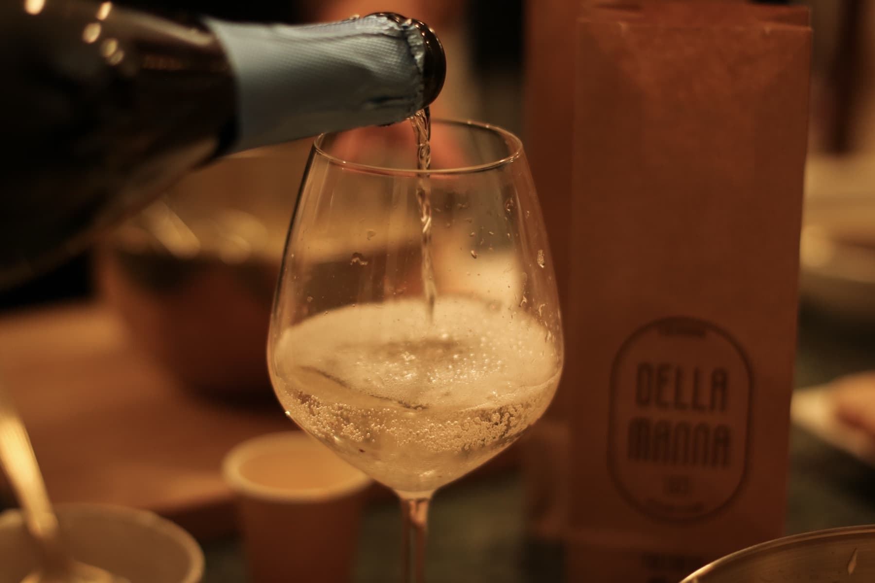 Prosecco poured beside a Della Manna coffee bag on the café counter