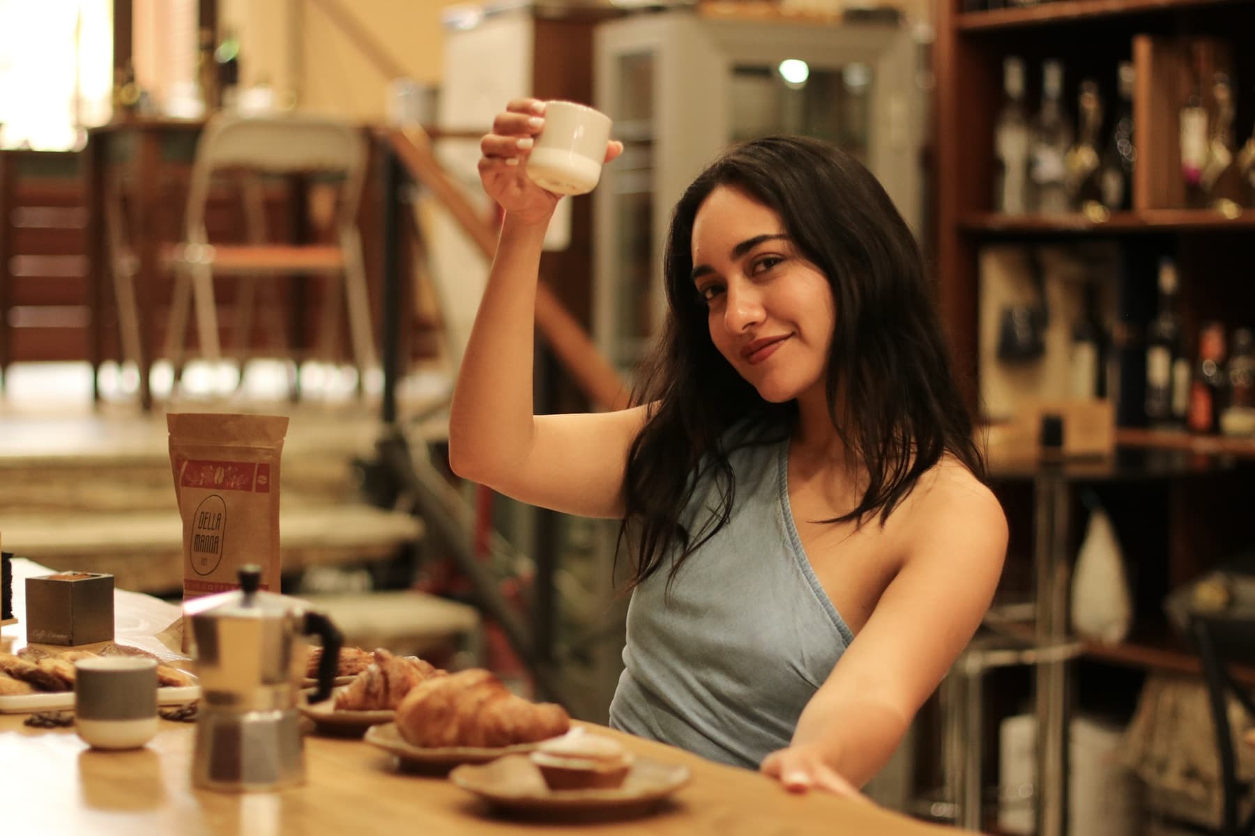 A guest raises a cappuccino at the café bar beside a moka pot, cornetti and a Della Manna coffee bag