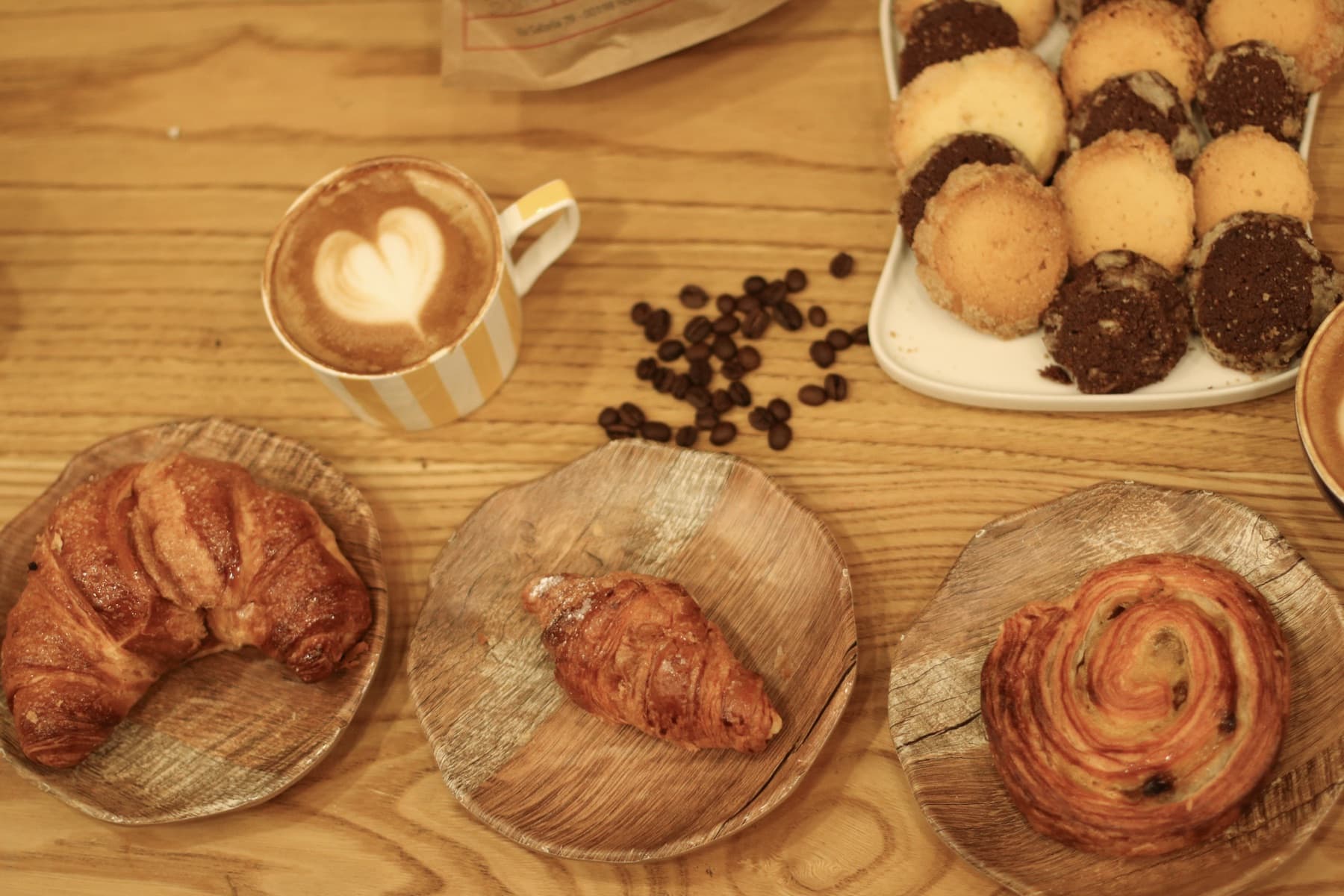 Overhead view of a cappuccino with latte art, coffee beans, cornetti and biscuits on a wooden café table