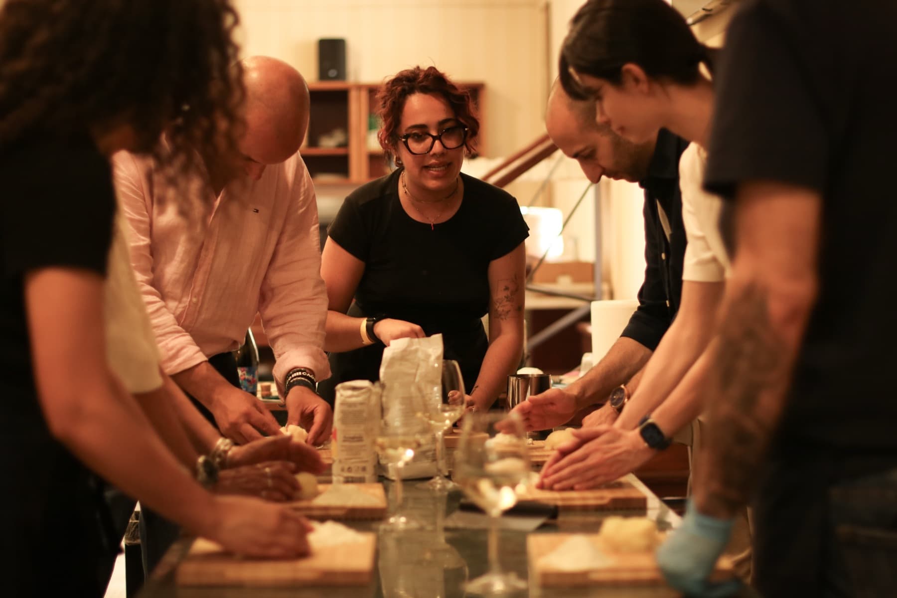 A small group shapes gnocchi dough on wooden boards at a long counter while the instructor watches from the centre