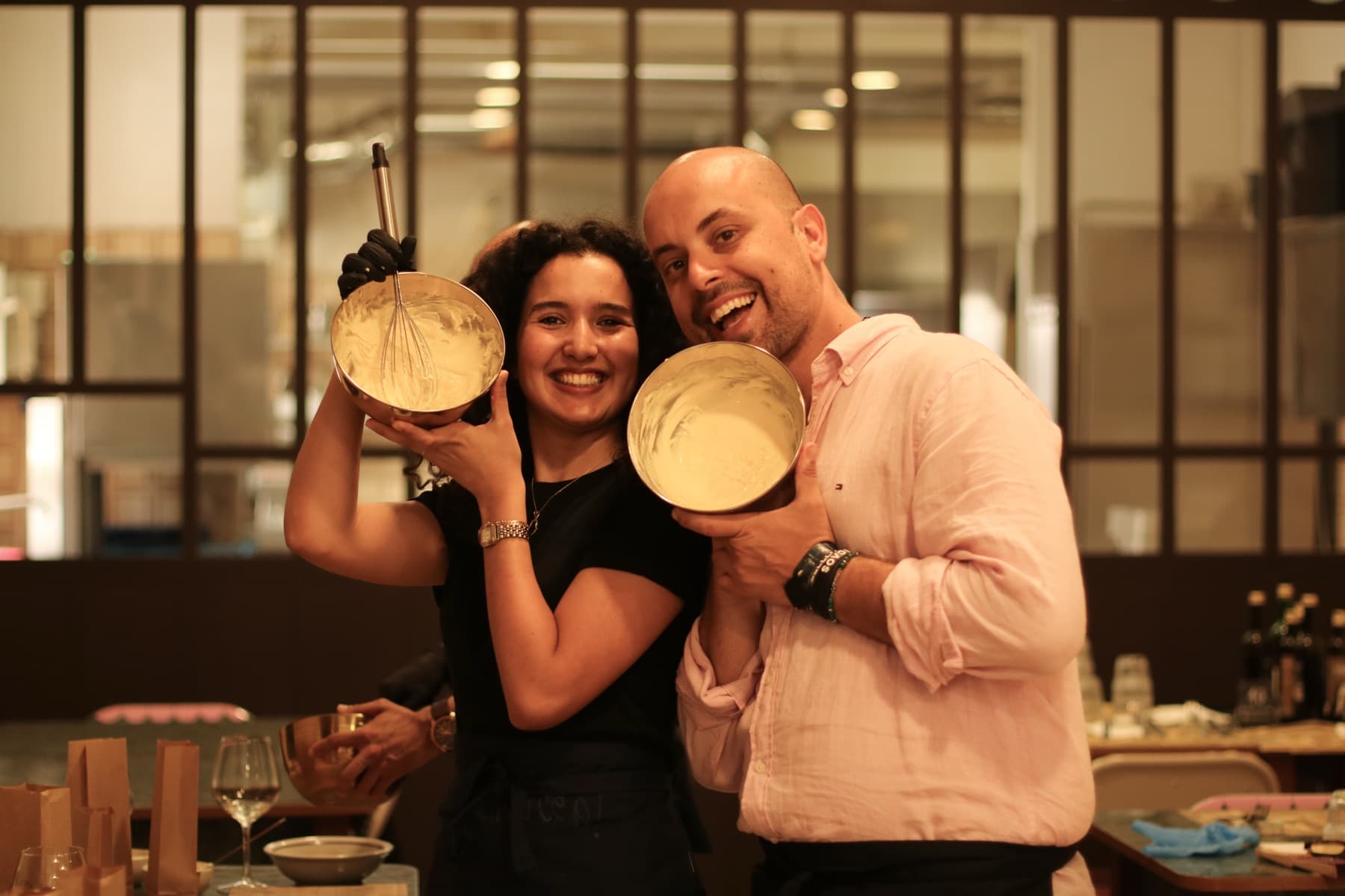 Two laughing guests hold up mixing bowls of whipped mascarpone cream during a cooking class in Rome