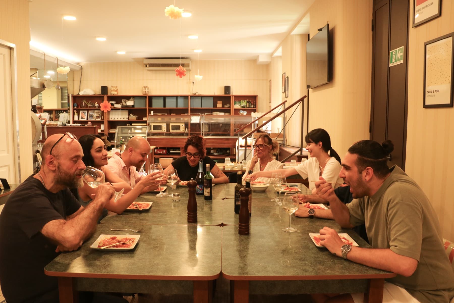 The whole group sits down together at a long table inside the café to eat the gnocchi they made, with wine